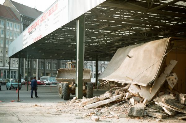 Ein Schuttberg unter dem Dach der Halle des Grenzübergangs, im Hintergrund läuft ein Mann zu einem Bulldozer.